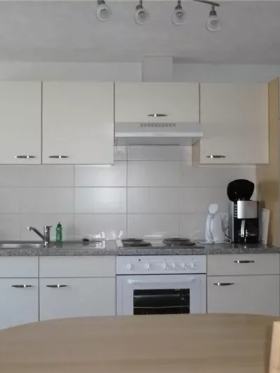 Eine moderne Küche mit hellen Schränken und einer funktionalen Ausstattung. Auf der Arbeitsfläche stehen ein Kochfeld, eine Spüle und eine Kaffeemaschine.