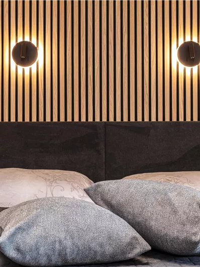 Een moderne slaapkamer met twee kussens en een stijlvolle houtbekleding. Aan de muur hangen ronde wandlampen die warm licht uitstralen.
