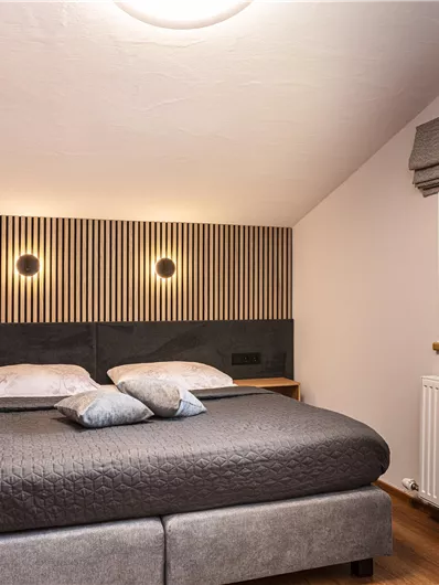 Een moderne slaapkamer met een groot bed en comfortabele kussens. De muren zijn eenvoudig gehouden, en de kamer heeft een aangename, lichte sfeer.