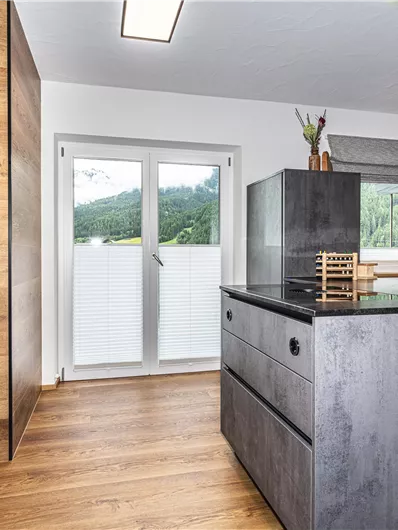 Een moderne keuken met hout- en betonaccenten. Grote ramen zorgen voor veel daglicht en een uitzicht op het groen.