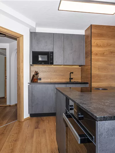 Een moderne keuken met grijze kasten en houten bekleding. Het keukeneiland heeft een zwart aanrechtblad en is uitgerust met een koffiepot.