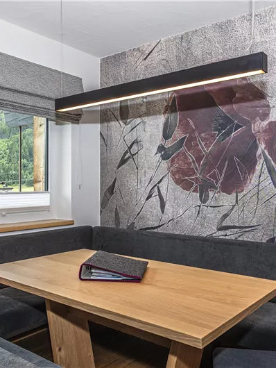 Een moderne eetkamer met een houten dienblad en comfortabele banken. De muur is versierd met een bloemmotief en een raam biedt uitzicht op de natuur.