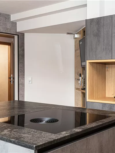 Een moderne keuken met een donker werkblad en elegante houten planken. De ruimte voelt uitnodigend en goed gestructureerd aan.