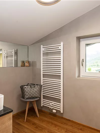 Een moderne badkamer met een elegant wastafel en houten vloer. Het heeft een raam en een handdoekradiator.