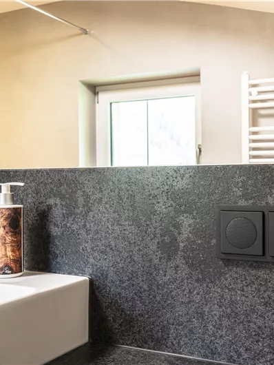 Een moderne badkamer met een elegant wastafel en een groot spiegeloppervlak. Op de achtergrond zijn radiatoren en elektrische aansluitingen en een radio zichtbaar.