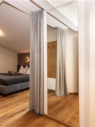 Een moderne slaapkamer met een groot bed en een houten vloer. Heldere kleuren en een raam zorgen voor een aangename sfeer.