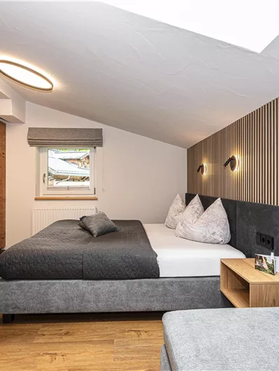 Een moderne slaapkamer met een tweepersoonsbed en gezellige houten wandbekleding. De ruimte is helder en vriendelijk ingericht, met een raam en een kleine werkplek.