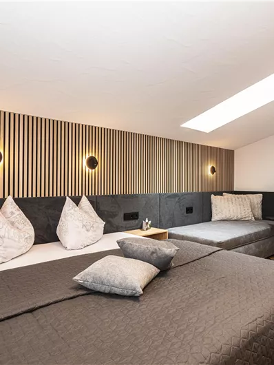 Een moderne slaapkamer met twee bedden en stijlvolle houten wandbekleding. Zachte verlichting en eenvoudige decoratie creëren een uitnodigende sfeer. Op de achtergrond staat een uitschuifbare bank.