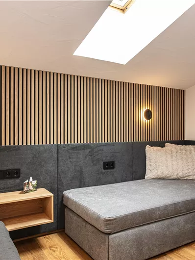 Een moderne kamer met een comfortabel bed en een kleurcontrast van grijs en hout. De muren zijn versierd met horizontale houten latten en er is sfeervolle verlichting. De bank nodigt uit tot genieten en ontspannen.