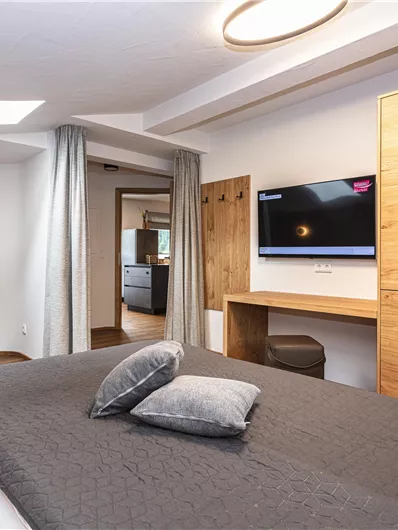 Een moderne slaapkamer met een groot bed en een gezellige bank. Aan de muur hangt een televisie en er staat een houten kast.