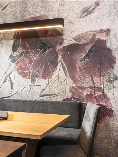 Een stijlvolle eetkamer met een houten bank en een tafel. De muur is versierd met een bloemmotief in zachte kleuren.