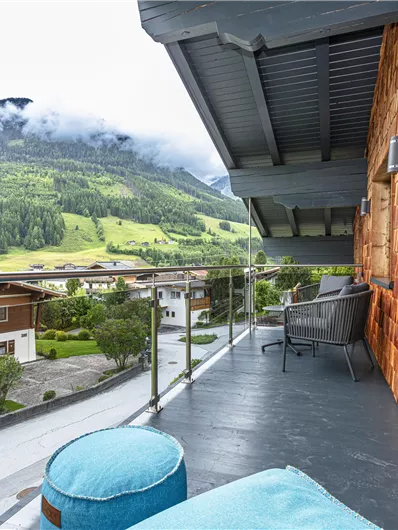Een balkon met uitzicht op groene bergen en wolken. De meubels en het relinggebied creëren een uitnodigende sfeer.