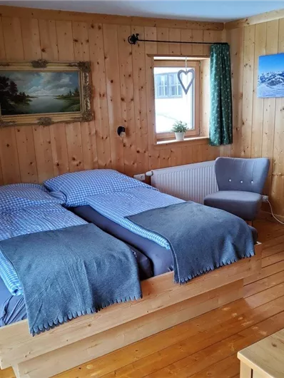Ein gemütliches Schlafzimmer mit Holzverkleidung. Zwei Einzelbetten, ein altmodisches Bild und ein kleiner Tisch mit einem Stuhl ergänzen den Raum.