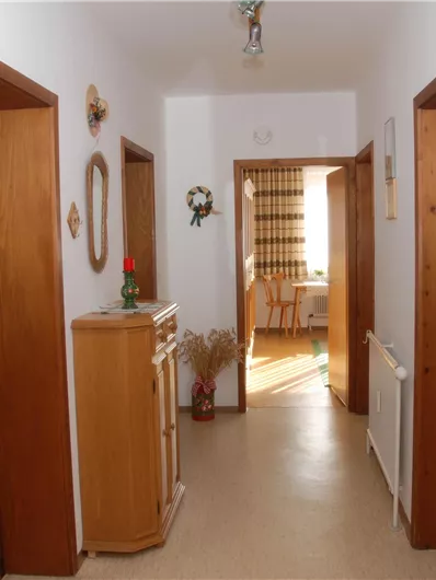 Ein heller Flur mit mehreren Türen und hellen Wänden. An der Seite hängen Garderobenhaken und ein Schrank steht im Raum.