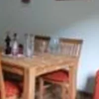 Ein gemütlicher Wohnraum mit einem Holztisch und Stühlen. Auf der rechten Seite befindet sich eine orangefarbene Couch und ein kleiner Fernseher an der Wand.