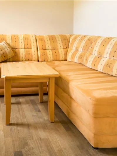 Een gezellig vertrek met een lichte, gestoffeerde bank en een kleine tafel. Op de achtergrond is een open deur te zien.