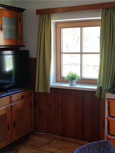 Ein gemütlicher Raum mit Holzvertäfelungen und einem Fenster. Ein Fernseher und eine Kommode sind ebenfalls zu sehen.
