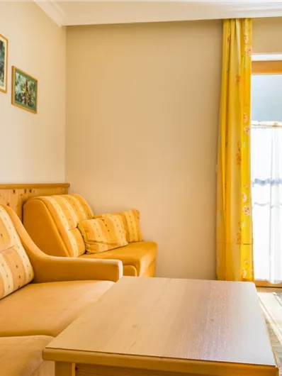 Een gezellige woonkamer met gele gordijnen en een houten tafel. De bank is comfortabel en voegt zich harmonieus in de lichte omgeving in.