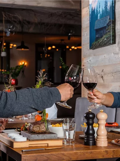 A smiling couple toasts with red wine in a cozy restaurant. The table is beautifully set with delicious dishes.