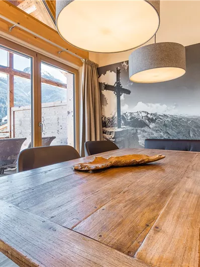 A cozy dining area with a wooden table and a comfortable corner bench. Large windows provide a beautiful view of the mountains.