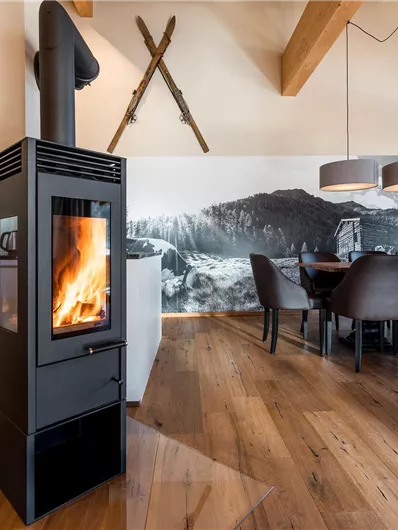 A modern living space with a stylish fireplace and a dining table. A large window area provides plenty of light and a view of beautiful wall decor.