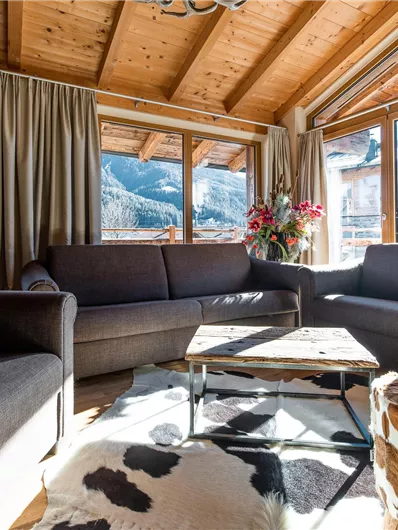 A cozy living space with modern sofas and a wooden table. Large windows offer a view of the mountains and let in plenty of light.