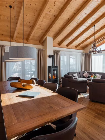 A modern living room with a wooden ceiling and large windows. A dining area with a table and stylish chairs invites you to linger.