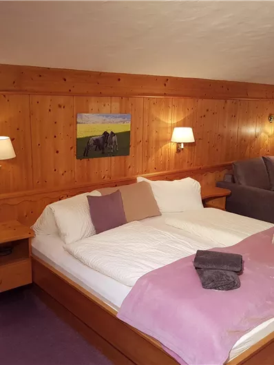 Ein gemütliches Schlafzimmer mit Holzverkleidung und sanften Farben. Es gibt ein großes Bett, eine Couch und Kunst an der Wand.