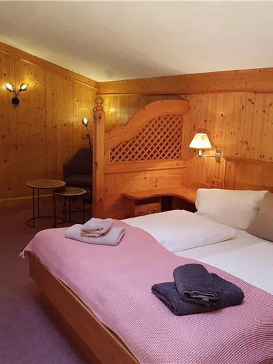 Ein gemütliches Schlafzimmer mit Holzwänden und einem Doppelbett. Die Einrichtung ist stilvoll und einladend, mit einem Fenster, das Tageslicht hereinlässt.