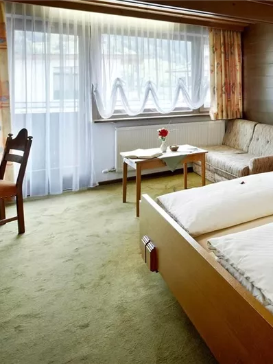 Een comfortabele hotelkamer met twee eenpersoonsbedden, een tafel en een televisie. Grote ramen zorgen voor veel daglicht en een uitnodigende sfeer.