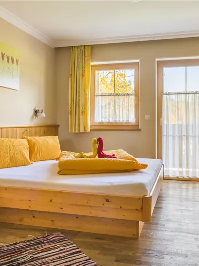 Een gezellige slaapkamer met een houten bed en lichte kleuren. Grote ramen laten veel licht binnen en creëren een uitnodigende sfeer.