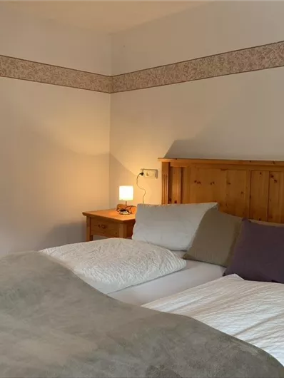 Ein gemütliches Schlafzimmer mit einem Doppelbett und weichen Kissen. Es gibt ein Nachttischchen mit einer Lampe und eine warme, einladende Atmosphäre.