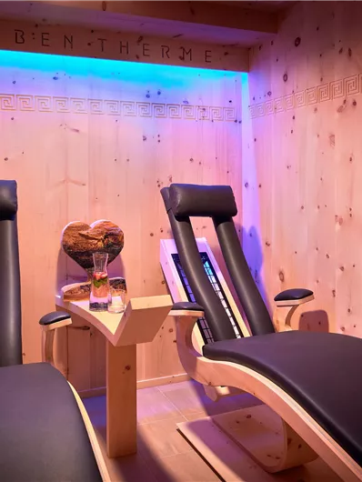Een gezellige wellnessruimte met twee comfortabele ligstoelen. De muren zijn van hout, en zacht licht creëert een ontspannende sfeer.