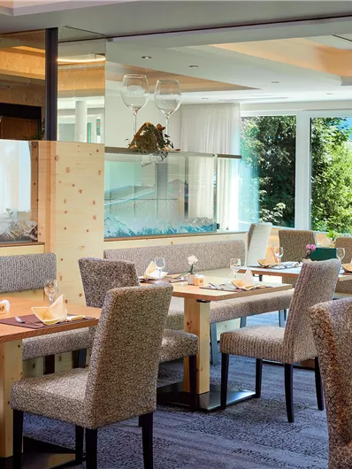 Een stijlvol restaurant met lichte muren en moderne tafels. Grote ramen bieden uitzicht op het groen en zorgen voor een uitnodigende sfeer.