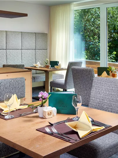 Een modern restaurant met elegante tafels en gezellige stoelen. Grote ramen bieden uitzicht op het groen en veel daglicht.