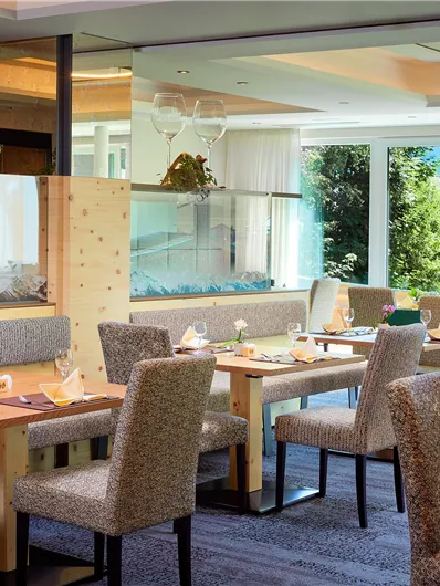Een elegant restaurant met moderne houten meubels en grote ramen. De tafels zijn prachtig gedekt en bieden uitzicht op de buitenlucht.