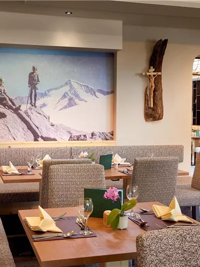 Een stijlvol restaurant met gezellige zithoeken en subtiele decoratieve elementen. Aan de muur hangt een groot schilderij van bergklimmers voor een indrukwekkend berglandschap.