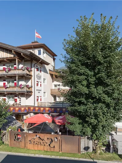 Een traditioneel Alpenhotel met meerdere balkons en bloemen. Omgeven door bomen en bergen, straalt het een uitnodigende sfeer uit.