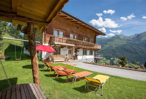 A beautiful wooden house on a meadow with a view of the mountains. Loungers and a swing invite you to relax.