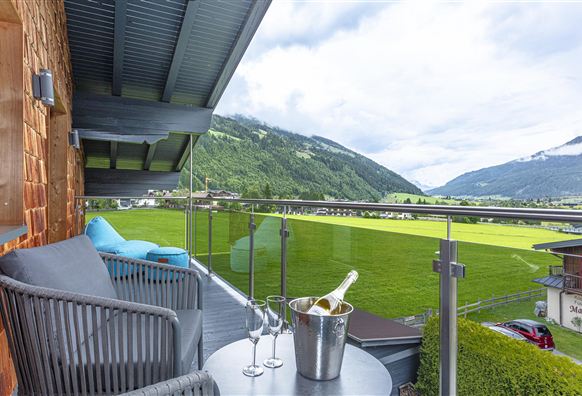 A beautiful, large balcony with a view of the green landscape and the mountains. On the table are two glasses and a champagne bucket.