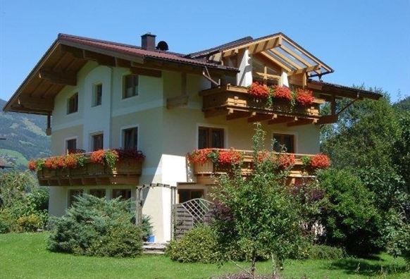 A beautiful house with flower balconies and a clear blue sky. Surrounded by green grass and trees.