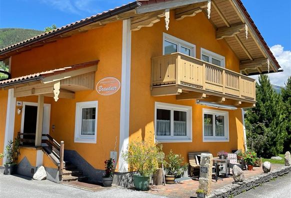 A charming orange house with a balcony.  
Surrounded by plants and a green landscape background.