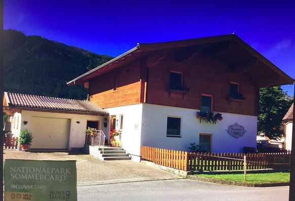 A cozy house with wooden siding and a light exterior paint. It is located in a rural area with a beautiful view of the mountains.