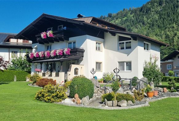 A beautiful house with a balcony and blooming plants. The garden is well-kept and surrounded by mountains.