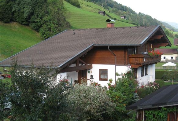 A beautiful house in a rural setting, surrounded by green hills. Colorful plants and trees adorn the garden.