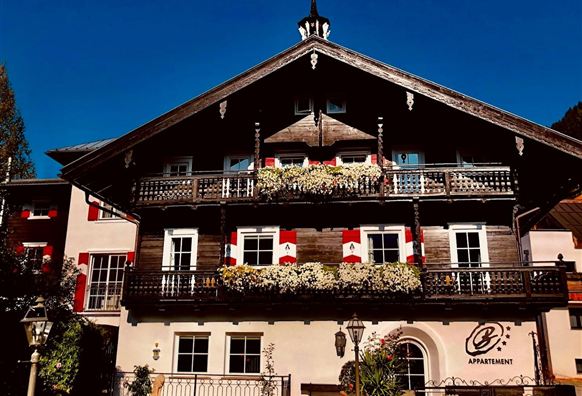 Ein traditionelles Alpenhaus mit schönem Holzbalustraden und blühenden Blumen. Der klare, blaue Himmel bildet einen tollen Kontrast zur Architektur.