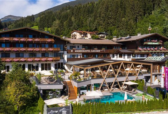 Ein modernes Hotel mit mehreren Etagen, umgeben von Bergen und Bäumen. Der großzügige Außenbereich umfasst einen Pool und gemütliche Terrassen.