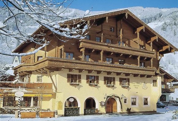 A charming wooden house in winter, surrounded by snow. The facade is yellow and has typical balcony decorations.