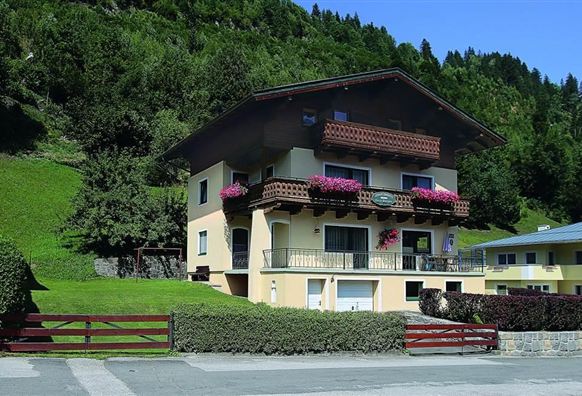 A beautiful house with balconies, surrounded by green hills. Colorful flowers adorn the windows, and the surroundings are calm and inviting.