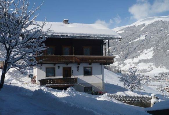 Ein schönes, schneebedecktes Berghaus mit traditioneller Architektur. Im Hintergrund sind schneebedeckte Berge und ein blauer Himmel zu sehen.